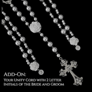 Puede incluir: Un cord&oacute;n de unidad de perlas blancas con detalles de rosas blancas, una cruz de metal plateado con cristales transparentes y dos dijes circulares grabados con las letras J y N. El texto ADD-ON: YOUR UNITY CORD WITH 2 LETTER INITIALS OF THE BRIDE AND GROOM es visible.