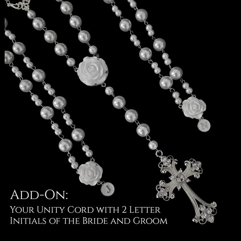 Puede incluir: Un cord&oacute;n de unidad de perlas blancas con detalles de rosas blancas, una cruz de metal plateado con cristales transparentes y dos dijes circulares grabados con las letras J y N. El texto ADD-ON: YOUR UNITY CORD WITH 2 LETTER INITIALS OF THE BRIDE AND GROOM es visible.