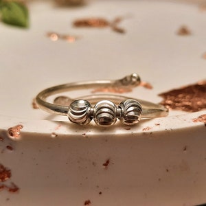 Puede incluir: Un anillo de plata con tres bolas texturizadas. El anillo está sobre una superficie blanca con motas de cobre.