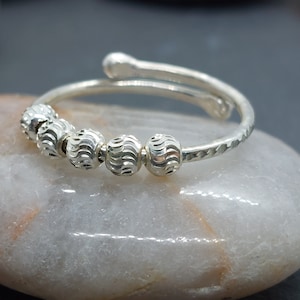 May include: A silver ring with a textured band and five round beads. The beads have a wavy pattern.
