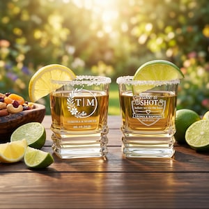 Puede incluir: Dos vasos de chupito personalizados con borde de sal, llenos de un líquido dorado y adornados con rodajas de limón y lima. Las copas están grabadas con iniciales, nombres y una fecha de boda. Un cuenco de madera con frutos secos y fruta deshidratada está cerca.