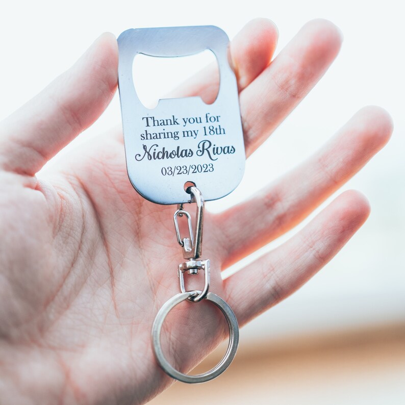 A personalized stainless steel bottle opener keychain, engraved with the text “Thank you for sharing my 18th,” held up close to the camera, with the keyring clearly attached.