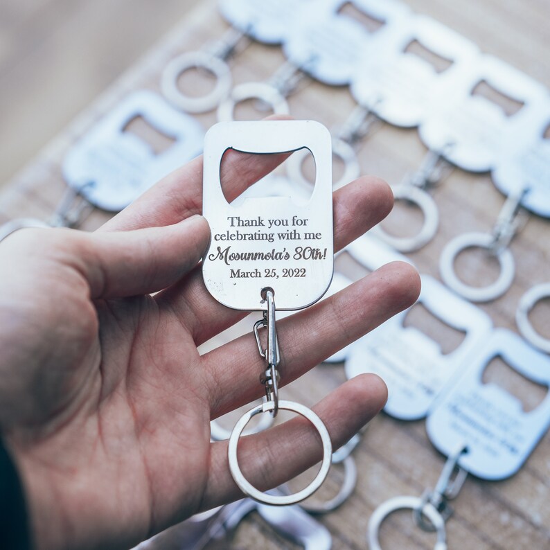 A hand holding a personalized stainless steel bottle opener keychain, with a clear view of the engraved thank you message and attached keyring, ready for use.