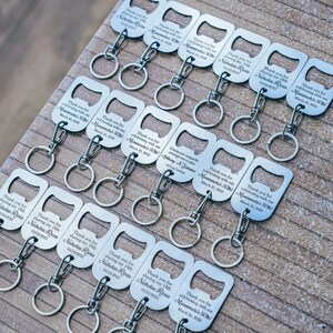 Several personalized stainless steel bottle opener keychains displayed on a wooden surface, emphasizing the uniformity and precision of the engravings.