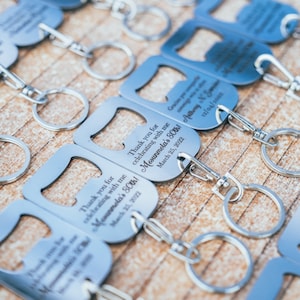 Close-up of multiple personalized stainless steel bottle opener keychains arranged neatly on a wooden surface, each engraved with a thank you message and personalized details.