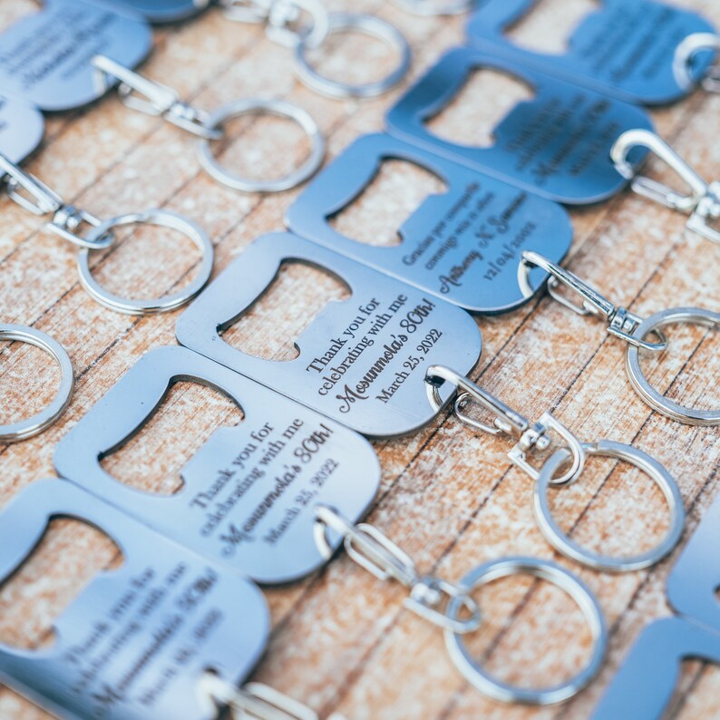 Close-up of multiple personalized stainless steel bottle opener keychains arranged neatly on a wooden surface, each engraved with a thank you message and personalized details.