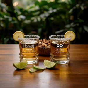 Può includere: Due bicchieri da whisky personalizzati con spicchi di limone e bordi salati. Un bicchiere recita "Cameron's 50th birthday celebration 09.07.2025". L'altro bicchiere recita "Cameron Old No. 21 Finally Legal 09.07.2025". È presente anche una ciotola di legno con noci e spicchi di lime.