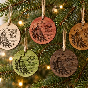 May include: Five circular wooden ornaments in varying shades of light, medium, and dark wood tones. Each ornament features a laser-engraved illustration of a lantern with pine branches and the text "LET YOUR LIGHT SHINE MATTHEW 5:16 CORNERSTONE CHURCH."