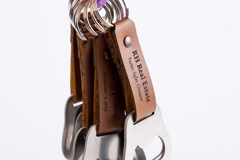 A bunch of leather-wrapped bottle opener keychains with brown leather wraps, hanging from a metal ring. The engraving on the leather is visible, showcasing the product’s portability.