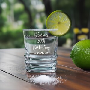 May include: A clear shot glass with a salt-rimmed edge, filled with liquid and a lime wedge. The glass is engraved with "Olivia's 30th Birthday 4.8.2025". A whole lime and a pile of salt are on the wooden surface.
