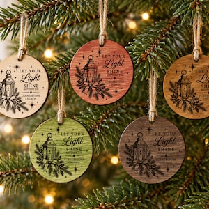 May include: Five circular wooden ornaments in varying shades of light, medium, and dark wood tones. Each ornament features a laser-engraved illustration of a lantern with pine branches and the text "LET YOUR LIGHT SHINE MATTHEW 5:16 CORNERSTONE CHURCH."