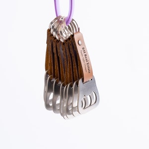 Another view of the leather-wrapped bottle opener keychains with brown leather wraps, hanging from a metal ring against a white background. The engraved text is clearly visible.