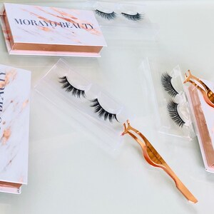Op de afbeelding: Een set valse wimpers in een transparante plastic verpakking met een roségouden wimperapplicator. De verpakking heeft een marmerpatroon met de tekst "MORAYO BEAUTY" erop gedrukt.