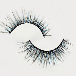 Op de afbeelding: Een paar valse wimpers met blauwe tips. De wimpers zijn zwart en hebben een natuurlijke, zwierige uitstraling.