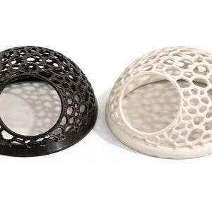 May include: Two decorative, dome-shaped objects. One is black, the other is off-white. Both have a honeycomb-like pattern with a large circular opening. The objects are on a white background.