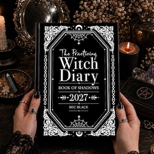 May include: A black hardback book titled The Practicing Witch Diary Book of Shadows 2027 by Bec Black. The cover features white decorative filigree, spider web illustrations, and geometric borders. The text is printed in a clear white serif font.