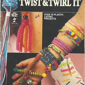 May include: Image of a book cover titled "Braid It, Curl It, Twist & Twirl It" with various colorful plastic lacing projects. The image showcases bracelets, earrings, and shoe decorations made with plastic lacing.
