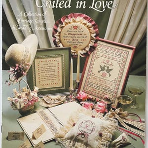 May include: A collection of marriage samplers and wedding accessories. The image features a variety of items, including framed samplers, a ring pillow, a hat, and a basket filled with small bags. The text "United in Love" is prominently displayed.