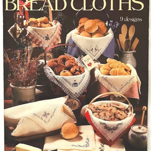 Peut inclure: Une couverture de livret vintage intitulée "BREAD CLOTHS" par Leisure Arts, présentant des paniers de produits de boulangerie garnis de linges brodés. La couverture comprend du texte et des illustrations de divers motifs, avec le nom de l'auteur en bas.