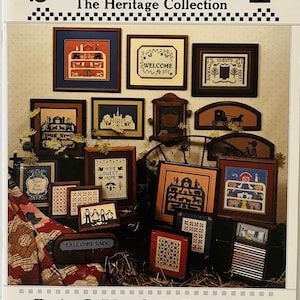 May include: A book titled "Scherenschnitte: The Heritage Collection" featuring a variety of cross-stitch designs with a country theme. The designs include a welcome sign, a house, a barn, a wagon, and a quilt. The book is part of the "Back Street Designs" collection and is book number 12.