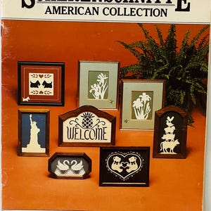 May include: A book cover for a Scherenschnitte American Collection featuring a variety of framed silhouette designs, including a welcome sign, a pineapple, a pair of swans, a pair of bears, a stack of farm animals, a pair of dogs, a silhouette of the Statue of Liberty, and a floral design. The book cover is orange with the title "Scherenschnitte American Collection" in black text.