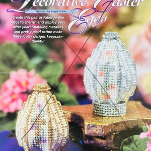 May include: Two decorative Easter eggs, one gold and one silver, are displayed on a gold-colored surface. The eggs are embellished with beads and intricate designs. The image includes text that reads "Decorative Easter Eggs" and describes the eggs as Fabergé-like.