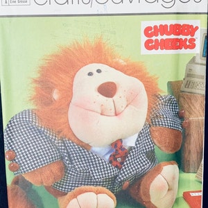 May include: A Simplicity crafts pattern for a lion plush toy. The pattern is titled "Chubby Cheeks" and features a lion wearing a black and white checkered suit with a red tie. The pattern is for one size.