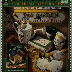 May include: A book cover for a painting project titled "Easy Painting for Home Decorating". The cover features a colorful illustration of a watering can, flower pots, a birdhouse, and a plate with a bee design. The book includes 20 projects to accessorize your home.