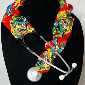 May include: A stethoscope with a red, yellow, and blue fabric stethoscope holder featuring a comic book print of superheroes.