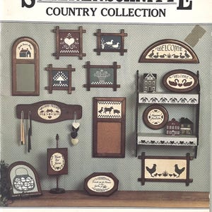 May include: A collection of country-themed wooden wall decor, including framed pictures, a mirror, a key holder, and a shelf. The designs feature folk art motifs such as hearts, ducks, houses, and chickens. The color palette is primarily brown, white, and black.