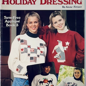 May include: A craft leaflet titled "Holiday Dressing" by Anne Fetzer. The leaflet features a white sweater with a red, white, and blue applique design, a red sweater with a Santa applique, a white sweater with a black cat and pumpkin applique, and a white sweater with a pink bunny and flower applique. The leaflet is part of the Leisure Arts Craft Leaflets series.