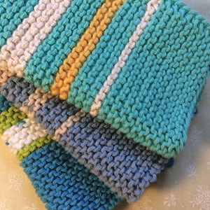 May include: A stack of four knitted dishcloths in various shades of blue, green, and white. The dishcloths are made with a textured stitch and have a striped pattern.