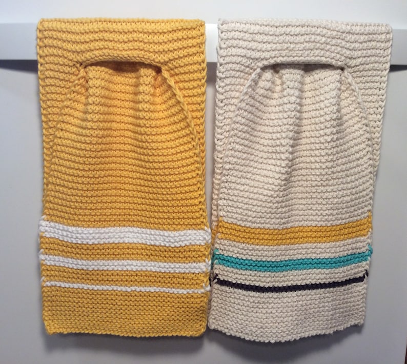 May include: Two knitted dishcloths hanging on a rack. The dishcloth on the left is yellow with white stripes. The dishcloth on the right is cream with a yellow stripe, a turquoise stripe, and a dark brown stripe.
