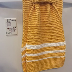 May include: A yellow knitted dish towel with white stripes hanging on a white door. The towel has a loop at the top for hanging.