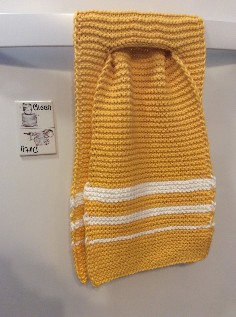 May include: A yellow knitted dish towel with white stripes hanging on a white door. The towel has a loop at the top for hanging.
