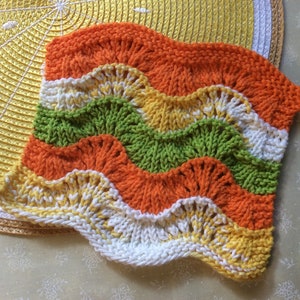 May include: A knitted dishcloth with a wavy pattern in orange, yellow, green, and white.