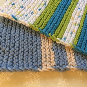 May include: Three knitted dishcloths in blue, green, white, and beige. The dishcloths are made with a textured stitch.