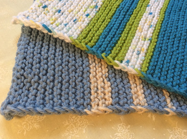 May include: Three knitted dishcloths in blue, green, white, and beige. The dishcloths are made with a textured stitch.