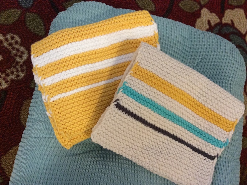 May include: Two knitted dishcloths with striped patterns. One dishcloth is yellow with white stripes, and the other is white with yellow, turquoise, and gray stripes.