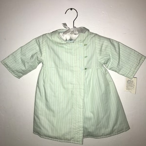 May include: A light green striped quilted baby coat with a white satin bow and buttons.