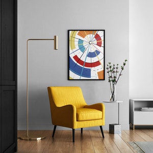 May include: A contemporary living room scene featuring a yellow armchair, a gold floor lamp, and a framed abstract art print. The artwork displays a circular design with red, blue, yellow, and orange segments. A small side table holds a vase of flowers.