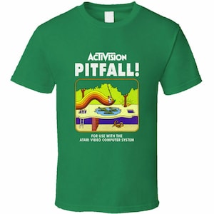 May include: Green t-shirt with a white graphic of the Atari video game Pitfall! The graphic features the game's title, a jungle scene, and the text "For use with the Atari Video Computer System".