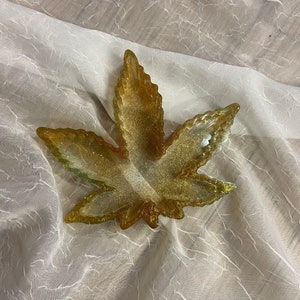 Könnte beinhalten: Ein goldfarbener, glitzernder Tablett in Blattform. Das Tablett ist aus Harz und hat eine glänzende Oberfläche.