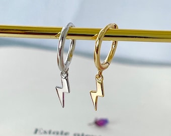 Pode incluir: Um par de brincos de argola com um pingente de raio. Um brinco é prateado e o outro é dourado.