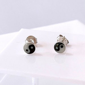 May include: A pair of silver stud earrings with a black and white yin yang symbol on each earring.