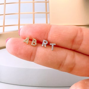 Könnte beinhalten: Vier kleine Buchstaben-Ohrstecker, die die Buchstaben A, B, R und T buchstabieren. Die Buchstaben sind mit kleinen, klaren Kristallen besetzt. Die Buchstaben A und B sind goldfarben, während die Buchstaben R und T silberfarben sind.