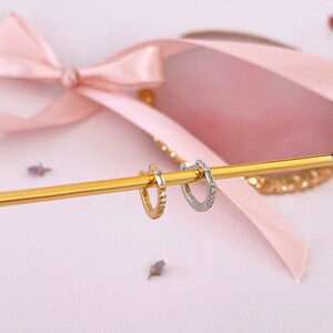 May include: Two small hoop earrings with a row of clear cubic zirconia stones. The hoop on the left is gold and the hoop on the right is silver.