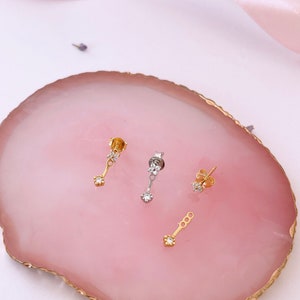 May include: Three gold earrings with small diamond accents. The earrings have a dangling design with a small diamond at the bottom of each earring.