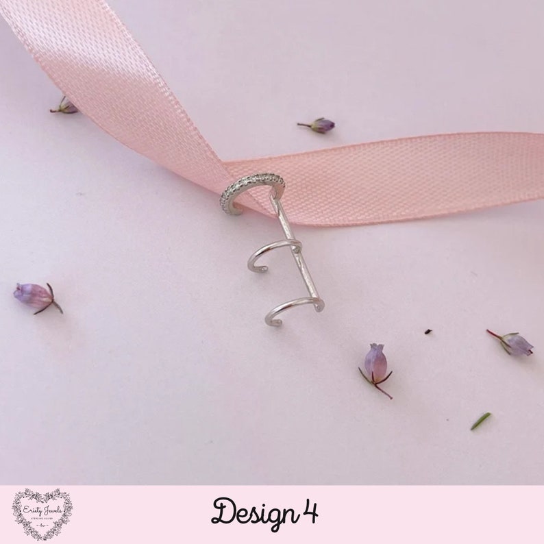 May include: Silver ear cuff with a triple hoop design and a single hoop with a row of small clear stones. The ear cuff is on a pink ribbon.