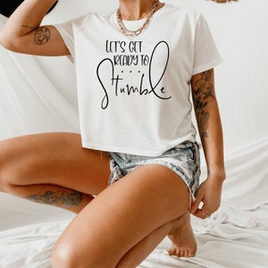 May include: White cropped t-shirt with the text "Let's get ready to stumble" in black lettering.